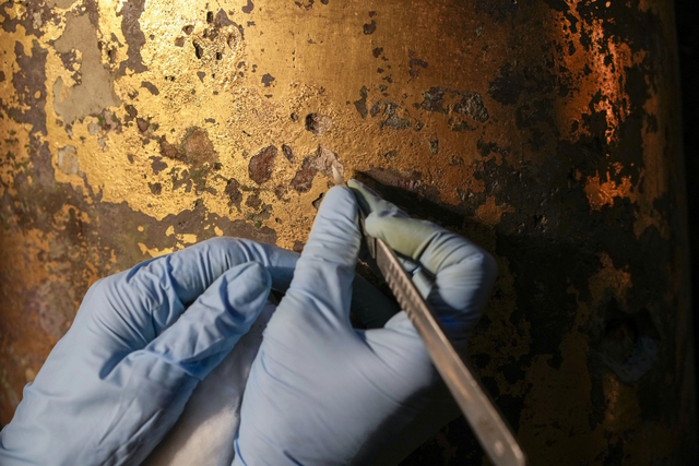 A close-up view of restoration work highlights the removal of centuries-old encrustations from the gold-coated surface.