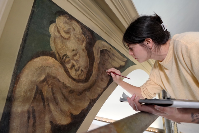 A conservator works meticulously to restore the intricate details of a cherubic angel mural at Old North Church.