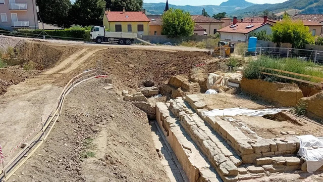 A panoramic view of the archaeological site in Sarsina, with visible remains of the capitolium temple amidst modern construction efforts.