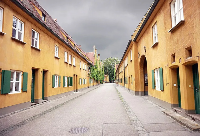 A quiet street within Fuggerei, lined with mustard-yellow facades and green-shuttered windows, reflecting over 500 years of tradition.