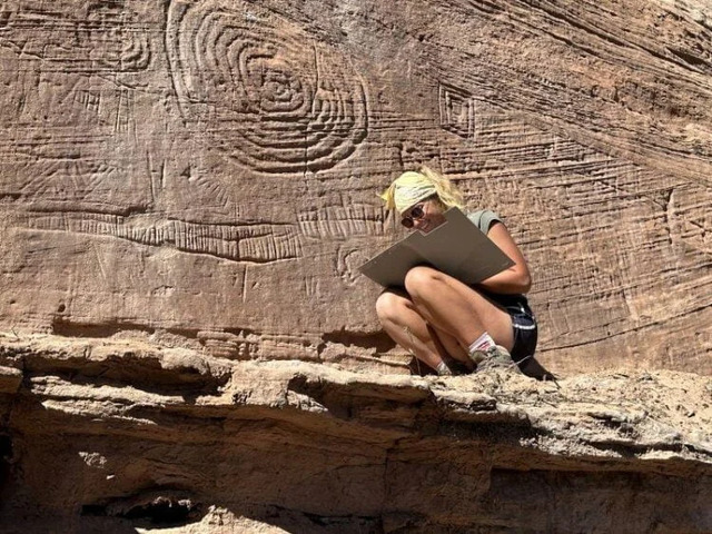 A researcher carefully sketches petroglyphs featuring large spiral designs on a cliff wall. These carvings hint at advanced astronomical knowledge. Credit: Jagiellonian University.