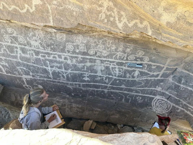 A team examines a rock panel densely covered with geometric and narrative carvings, including hunting scenes and tribal motifs. Credit: Jagiellonian University.