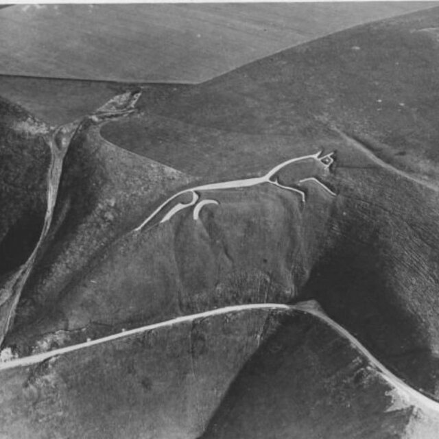 An archival black-and-white aerial photograph of the Uffington White Horse, capturing its historic form against the natural landscape.