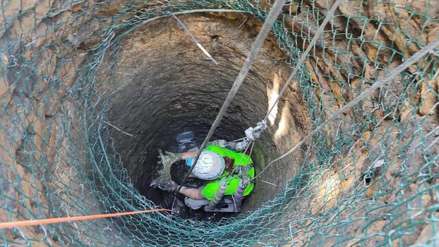 Another perspective of the archaeologist descending the well, showcasing the meticulous efforts required to retrieve ancient artifacts safely.