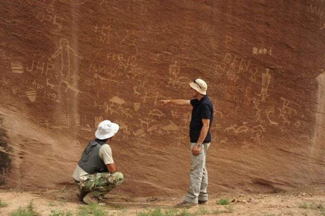 Archaeologists discuss and analyze a rock art panel displaying hunting scenes and tribal symbols, possibly representing cultural narratives. Credit: Jagiellonian University.