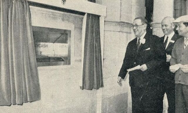 Barclays’ bank manager on Enfield High Street tests out the world’s first cash machine, joined by Reg Varney (wearing the golf cap). Image courtesy of Barclays.