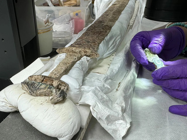 Conservation experts carefully work on the sixth-century sword, highlighting its silver-and-gilt hilt and leather-and-wood scabbard. Credit: Prof Alice Roberts/BBC/Rare TV.