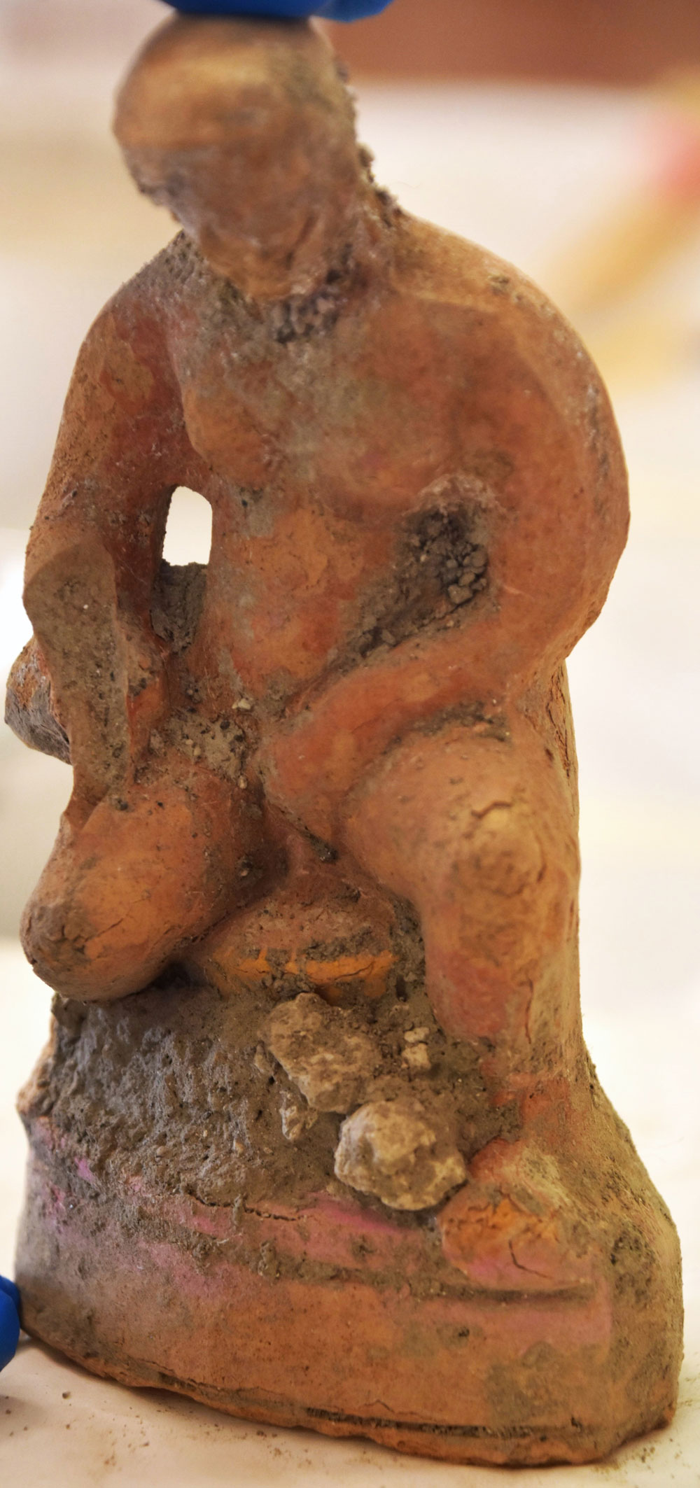 A seated terracotta figure, intricately designed and partially restored, possibly representing a symbolic or mythological figure related to fertility or seasonal cycles.