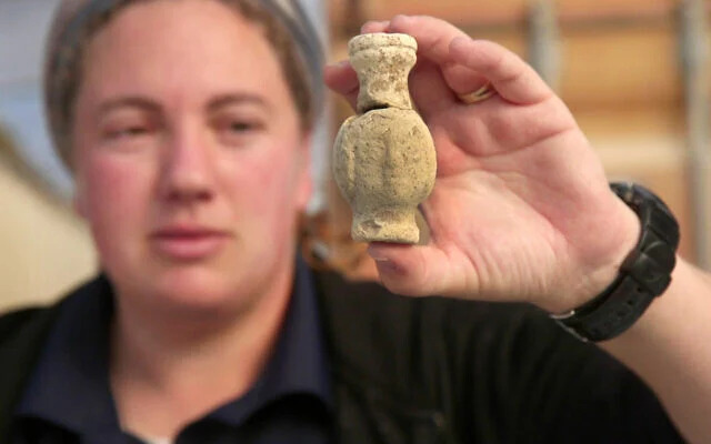 IAA archaeologist Shira Lifshitz holds a small ceramic bottle discovered at the Byzantine monastery excavation near Kiryat Gat, a glimpse into ancient daily life. (Emil Aladjem/Israel Antiquities Authority, January 6, 2024)