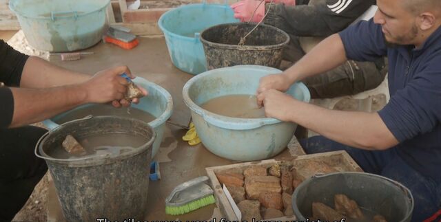 Researchers cleaning and analyzing Roman-era roof tiles, some stamped with the emblem of the VIth Legion, used for various purposes within the military base.