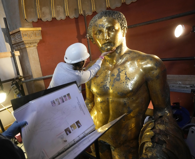 Restorers analyze and refer to detailed notes while delicately treating the gilded bronze statue's features.