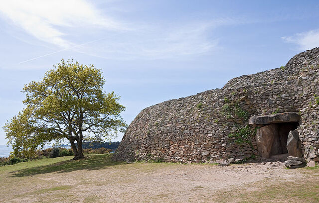 The entrance to the Gavrinis Passage Tomb features beautifully carved entrance slabs and the beginnings of a tunnel, with the stone mound partially exposed.