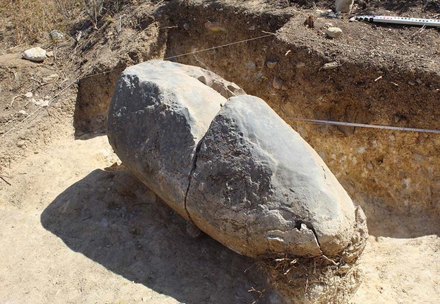 The menhir, partially unearthed, showing visible cracks and evidence of age.